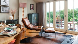 A spacious living room with a leather chair, a piano, and a view of a lush garden through large sliding glass doors. - Higher Mapstone in Lustleigh (Newton Abbot)