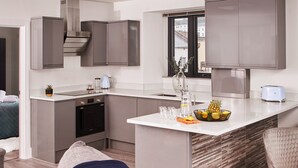 A modern kitchen with grey cabinets, a central island, and a dining area with a chair. - Harbour Breeze in Torquay (Torquay)