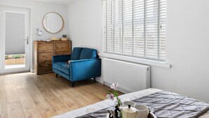 Ein Schlafzimmer mit einem Bett, einem Schminktisch, einem Stuhl, einem Fenster mit Jalousien und einer Tür zu einem Außenbereich.