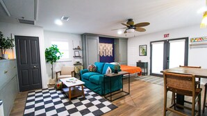 A living room with a checkered rug, a blue sofa, a wooden coffee table, and a dining table with chairs.