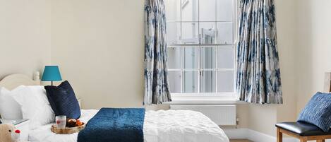 Une chambre d’hôtel avec deux lits, une fenêtre avec des rideaux, une lampe, un ours en peluche et un panier.