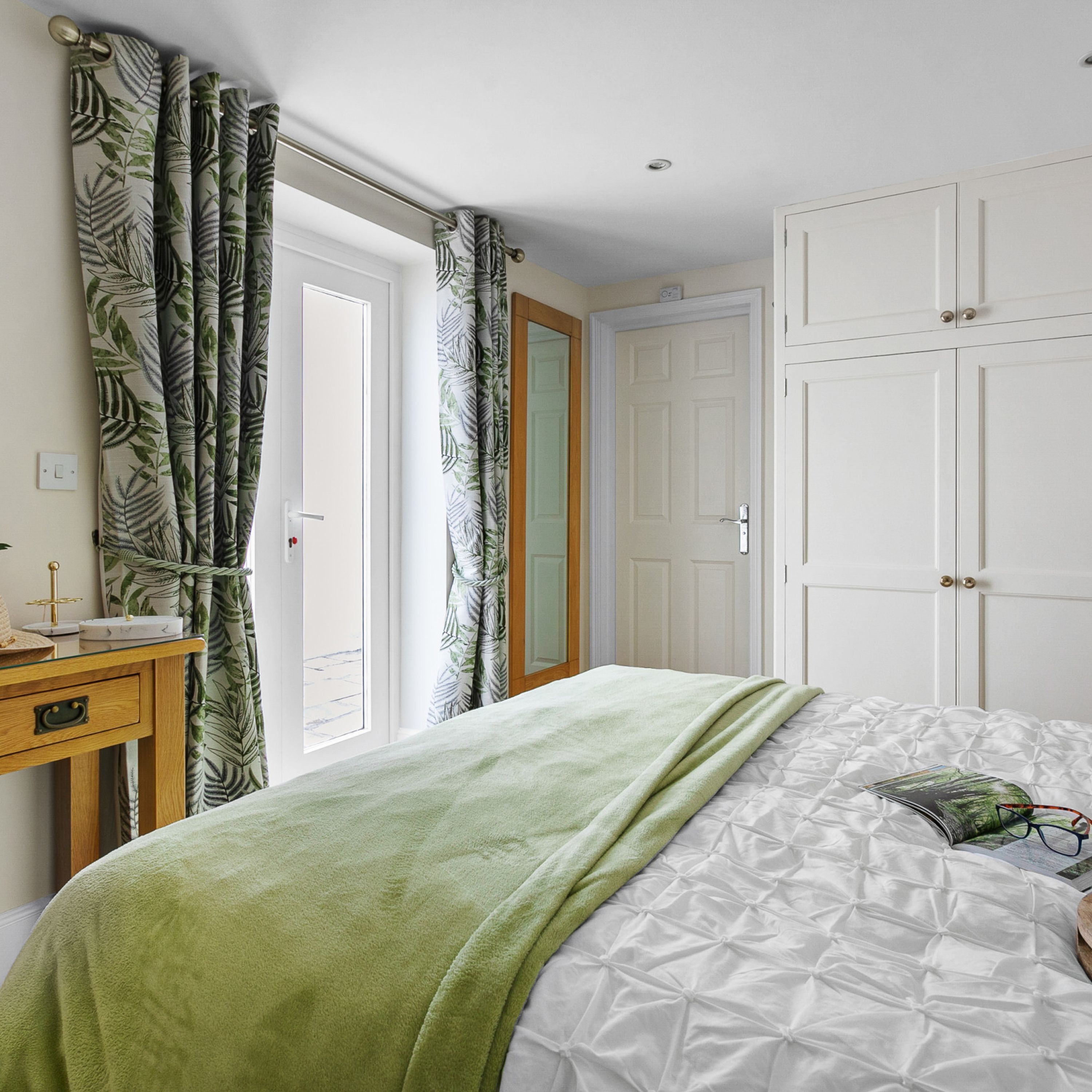 A bedroom with a bed, a bedside table, a mirror, and a wardrobe.
