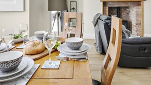 Un coin repas avec une table en bois dressée pour le repas, une cheminée et une horloge au mur.