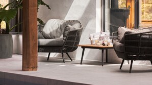 A modern outdoor seating area with wicker furniture and a table, featuring a large window and a view of the outdoors. - Swifts Return in Lower Ashton (Newton Abbot)