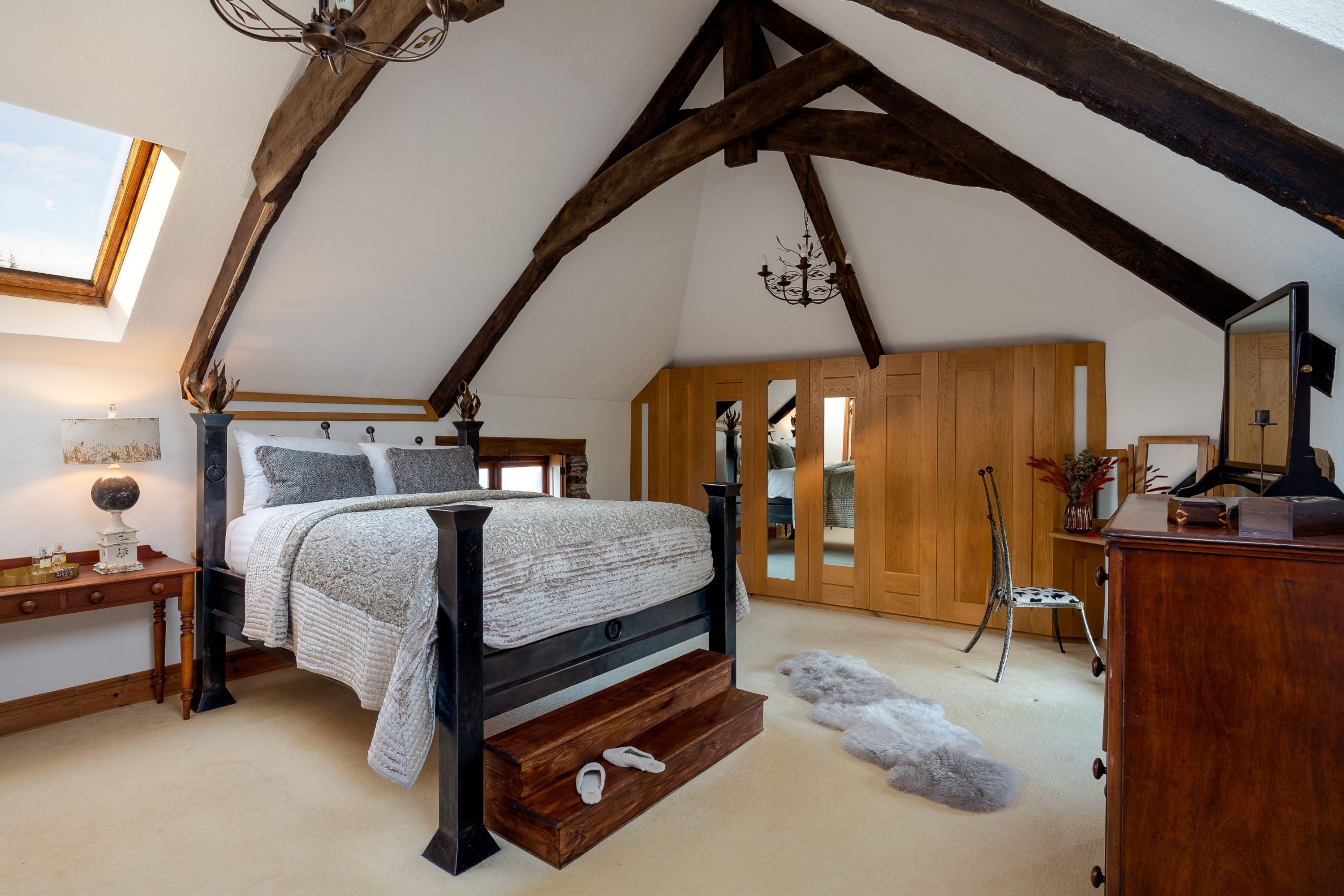 A bedroom with a sloped ceiling, a bed with a wooden headboard, a nightstand, a dresser, and a mirror.