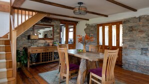 A dining area with a wooden table, chairs, and a vase of flowers. There is a staircase with wooden railings leading to another room. - Old Coach House in Berry Pomeroy (Totnes)