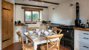 A kitchen with wooden cabinets, a stove, and a dining table set with plates and bowls. - Old Coach House in Berry Pomeroy (Totnes)