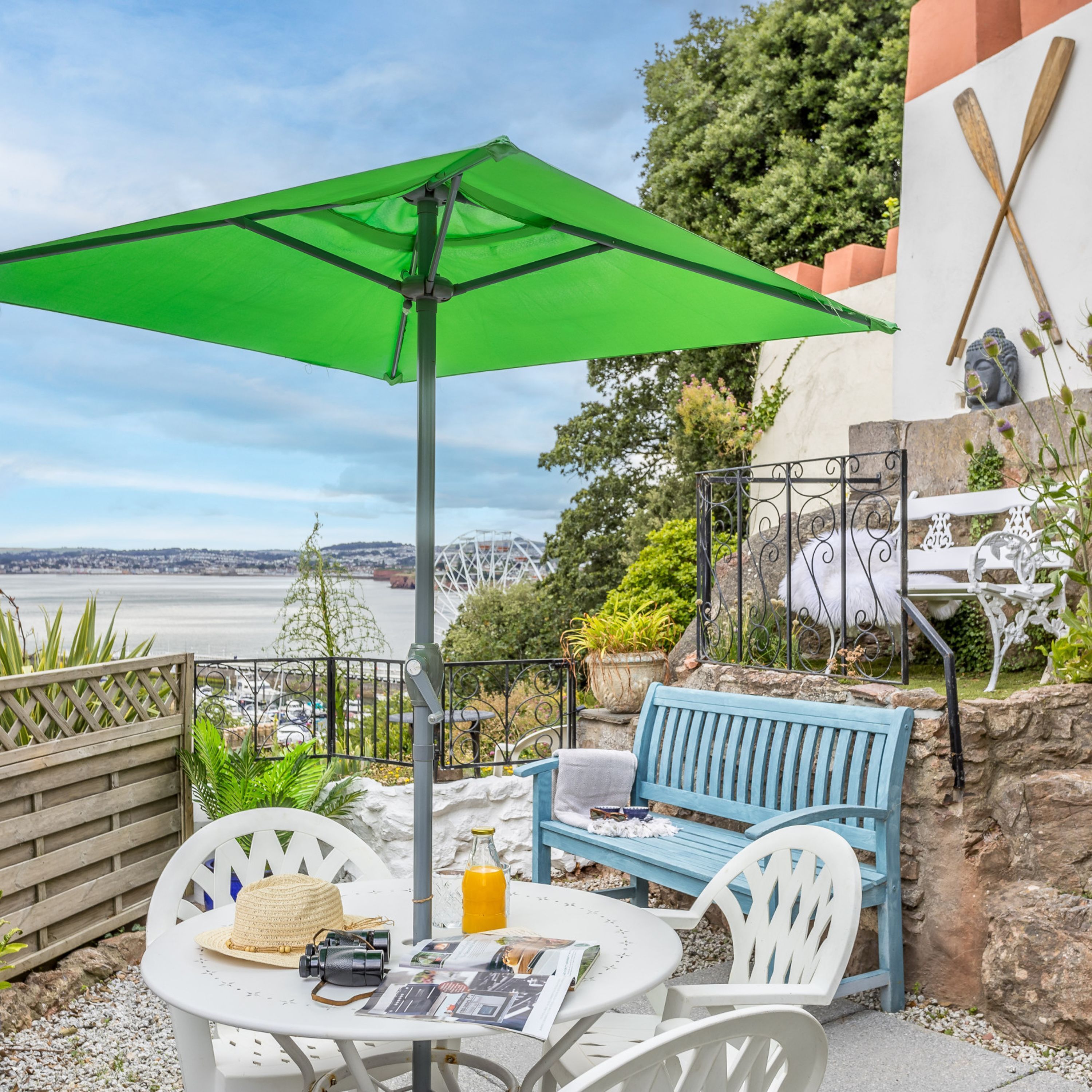 Un patio con mesa, sillas, un paraguas verde y vista al agua.