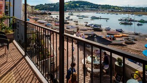 A balcony with a view of boats on a harbor, a table with people dining, and a building in the background. - Crab Shack in Teignmouth (Teignmouth)