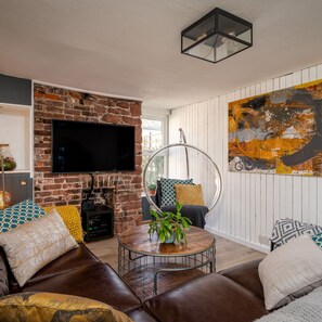 Sala de estar con chimenea de ladrillo, sofá de cuero y una mesa redonda para café con una planta.