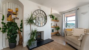 A living room with a fireplace, a sofa, and various plants. - Crab Shack in Teignmouth (Teignmouth)