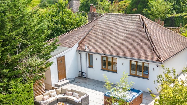 Una casa con techo de tejas, un patio con mobiliario exterior y un jacuzzi.