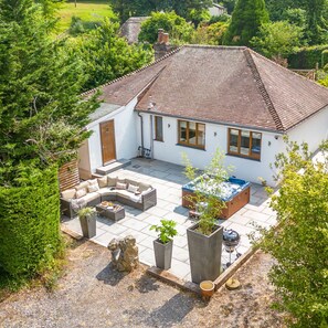 Una casa con techo de tejas, un patio con mobiliario exterior y un jacuzzi.