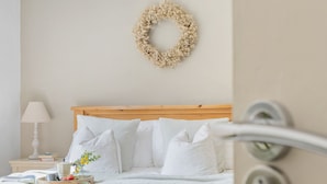 Un dormitorio con una cama de madera, ropa de cama blanca, una mesita de noche con lámpara y un arreglo en la pared.