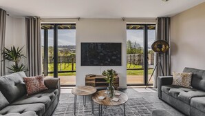 A modern living room with a sofa, coffee table, and TV, featuring a large window with a view of greenery.