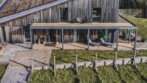 A modern house with a large deck, a covered patio, and a view of the countryside.