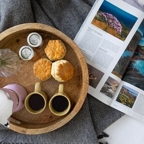 A wooden tray with biscuits, honey jars, and two mugs of tea, alongside a magazine with travel photography. - Greenacre in Bishopsteignton (Teignmouth)