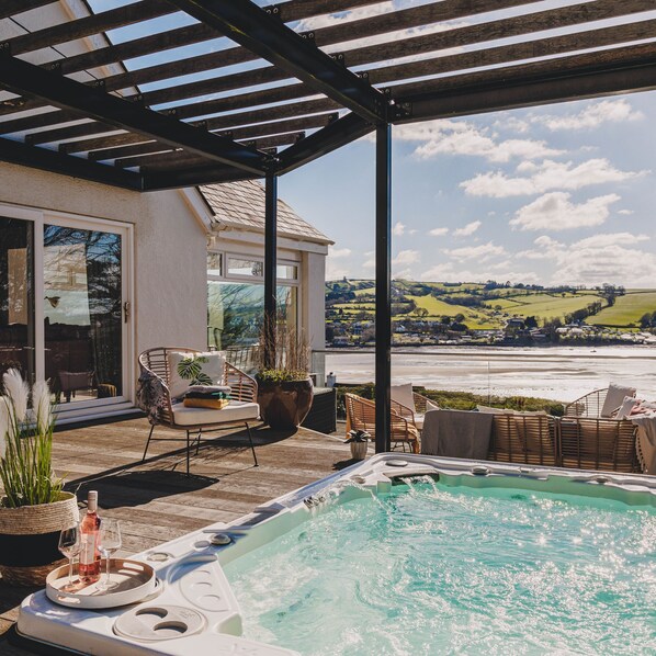 A covered outdoor area with a hot tub, lounge chairs, and a view of the sea.
