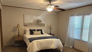 A bedroom with a bed, two bedside tables, a ceiling fan, a window with curtains, and a painting on the wall. - A getaway on the Marsh! (Murrells Inlet)