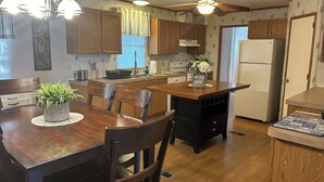 A kitchen with wooden cabinets, a central island, a dining table with chairs, and a ceiling fan. - A getaway on the Marsh! (Murrells Inlet)