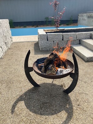 A fire pit with a circular metal frame and a flat stone base, surrounded by gravel. - Vacation home with a private pool (Soltau)