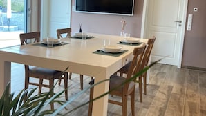 Un espace repas moderne avec une grande table, des chaises et un téléviseur à écran plat fixé au mur.