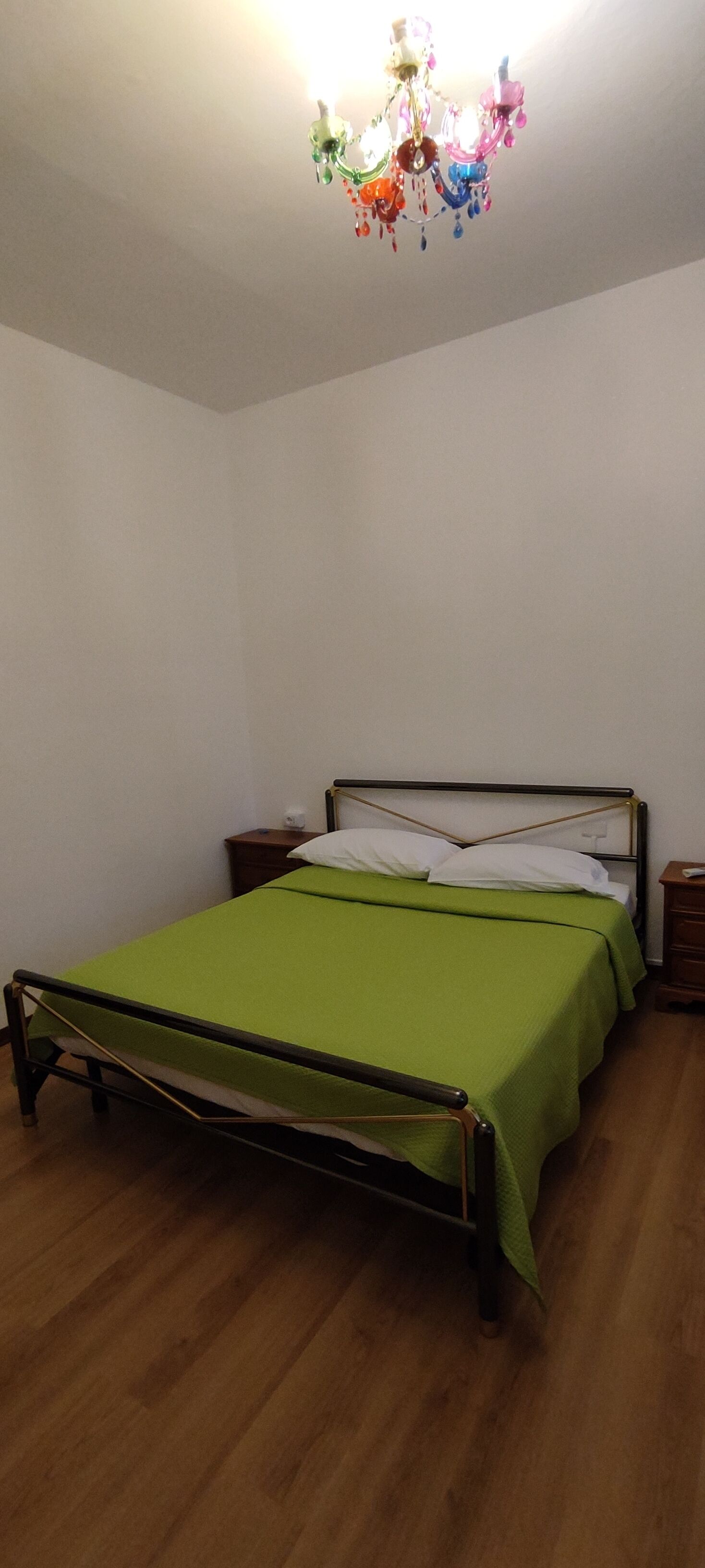 A single bed with a green bedspread in a room with wooden flooring and white walls.