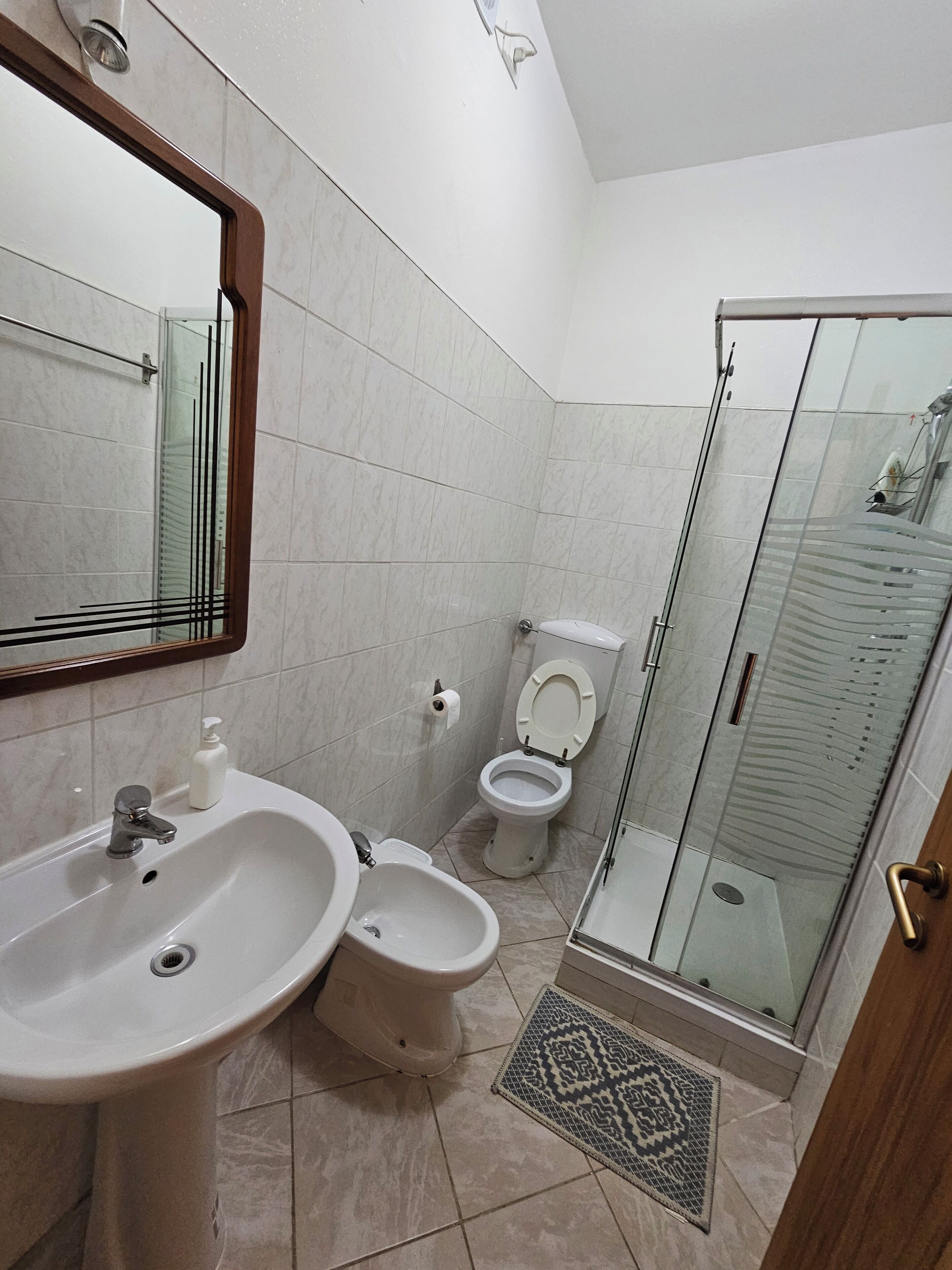 A bathroom with a sink, bidet, toilet, and a glass shower enclosure.
