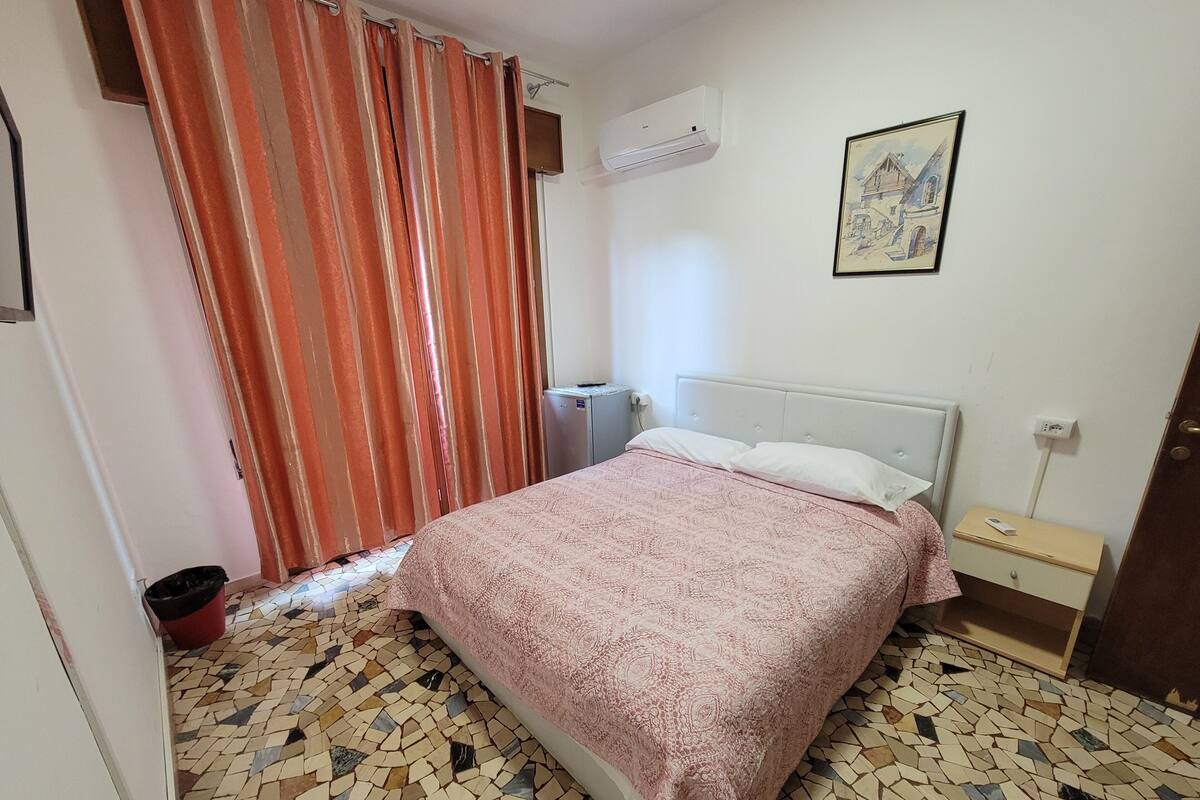 Une chambre à coucher avec un lit, une table de chevet, un radiateur, un tableau et un sol carrelé.