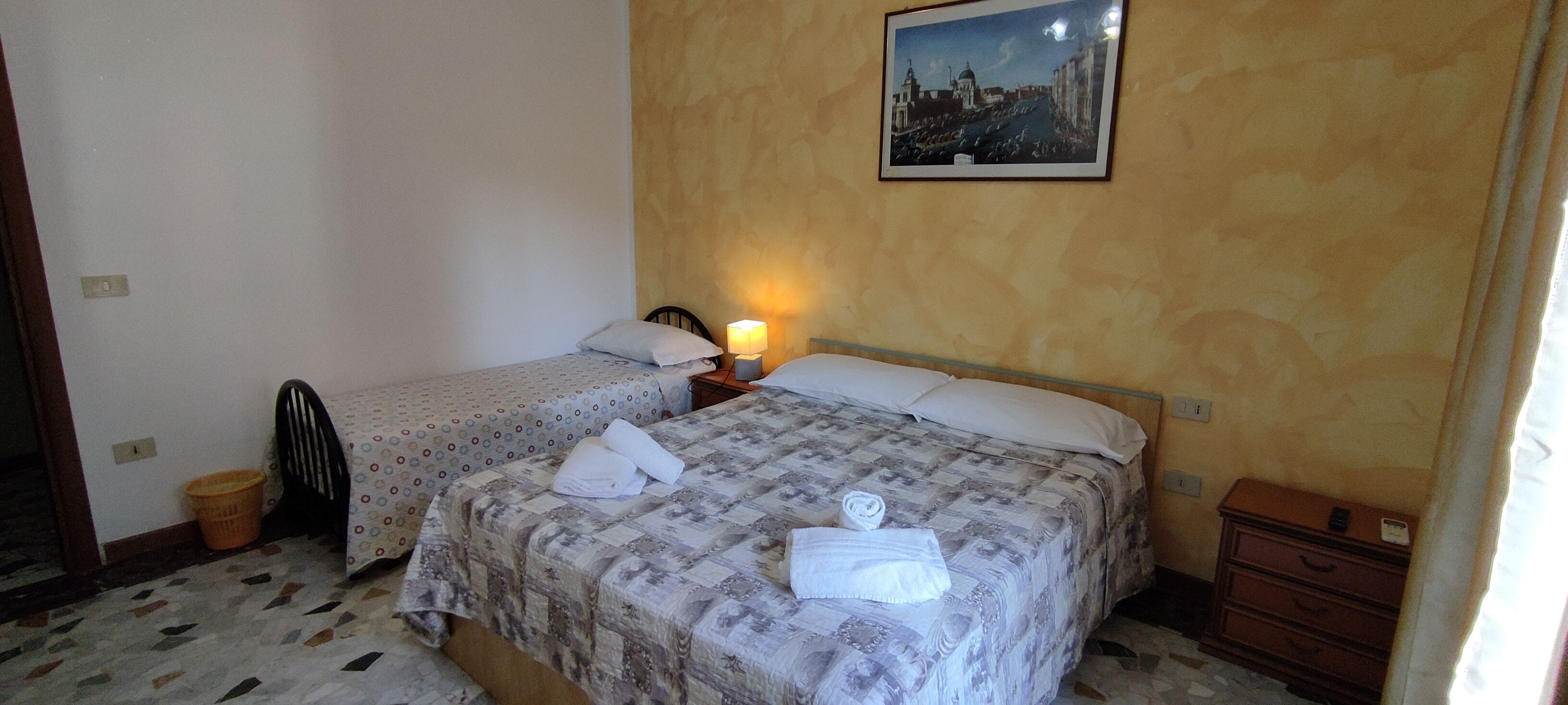 Une chambre d’hôtel avec deux lits, une table de chevet avec une lampe, une commode et un tableau encadré au mur.