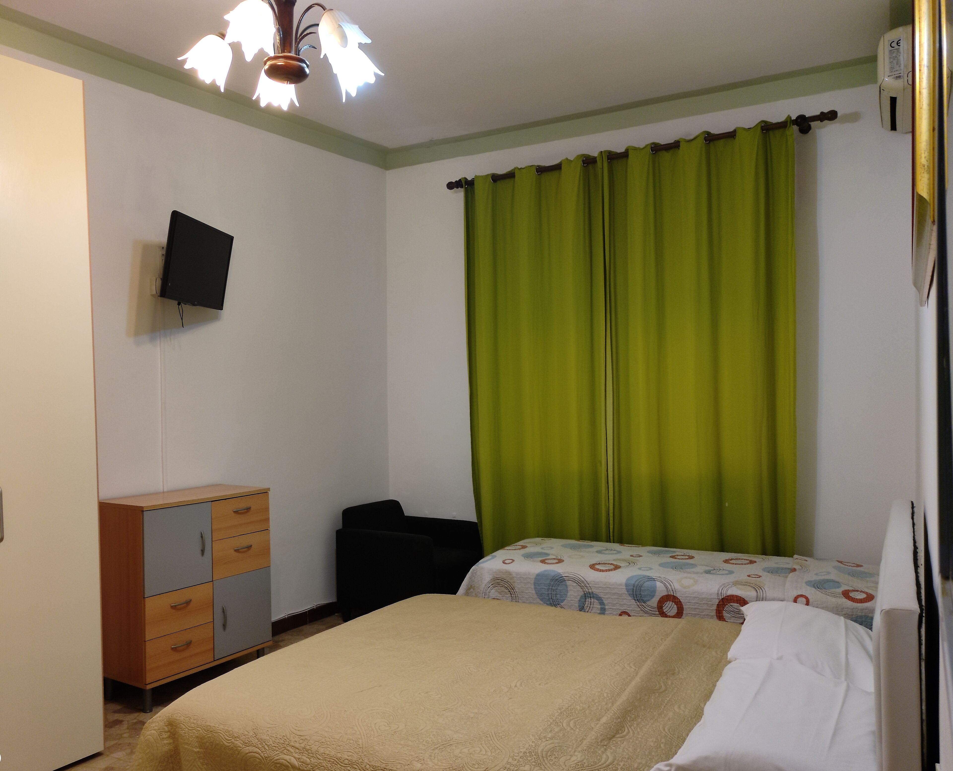 Une chambre à coucher avec un lit, une commode, un téléviseur et un rideau vert.