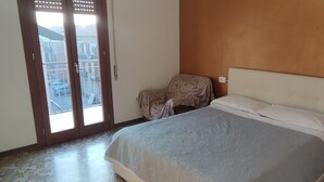 Ein Schlafzimmer mit einem Bett, einem Sessel, einem Nachttisch und einer Tür zu einem Außenbereich.