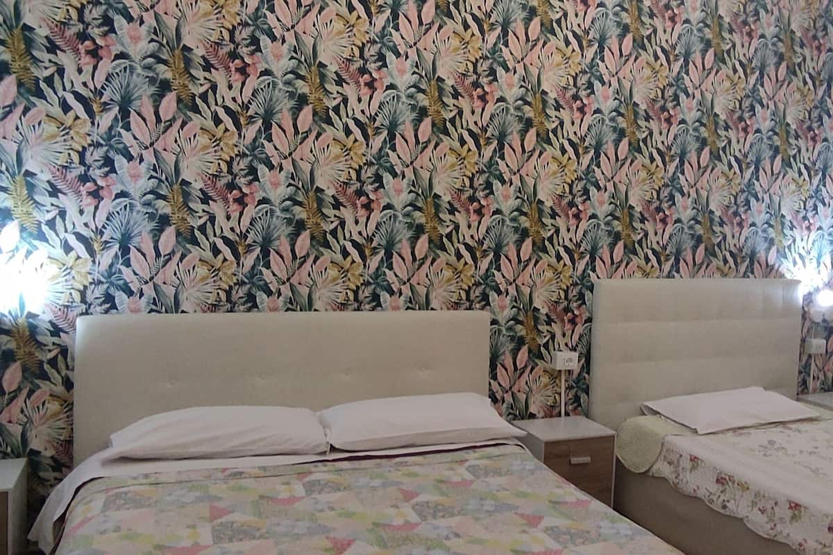 Une chambre avec deux lits, une tête de lit à motifs floraux, des tables de chevet avec des lampes et une fenêtre avec des stores.