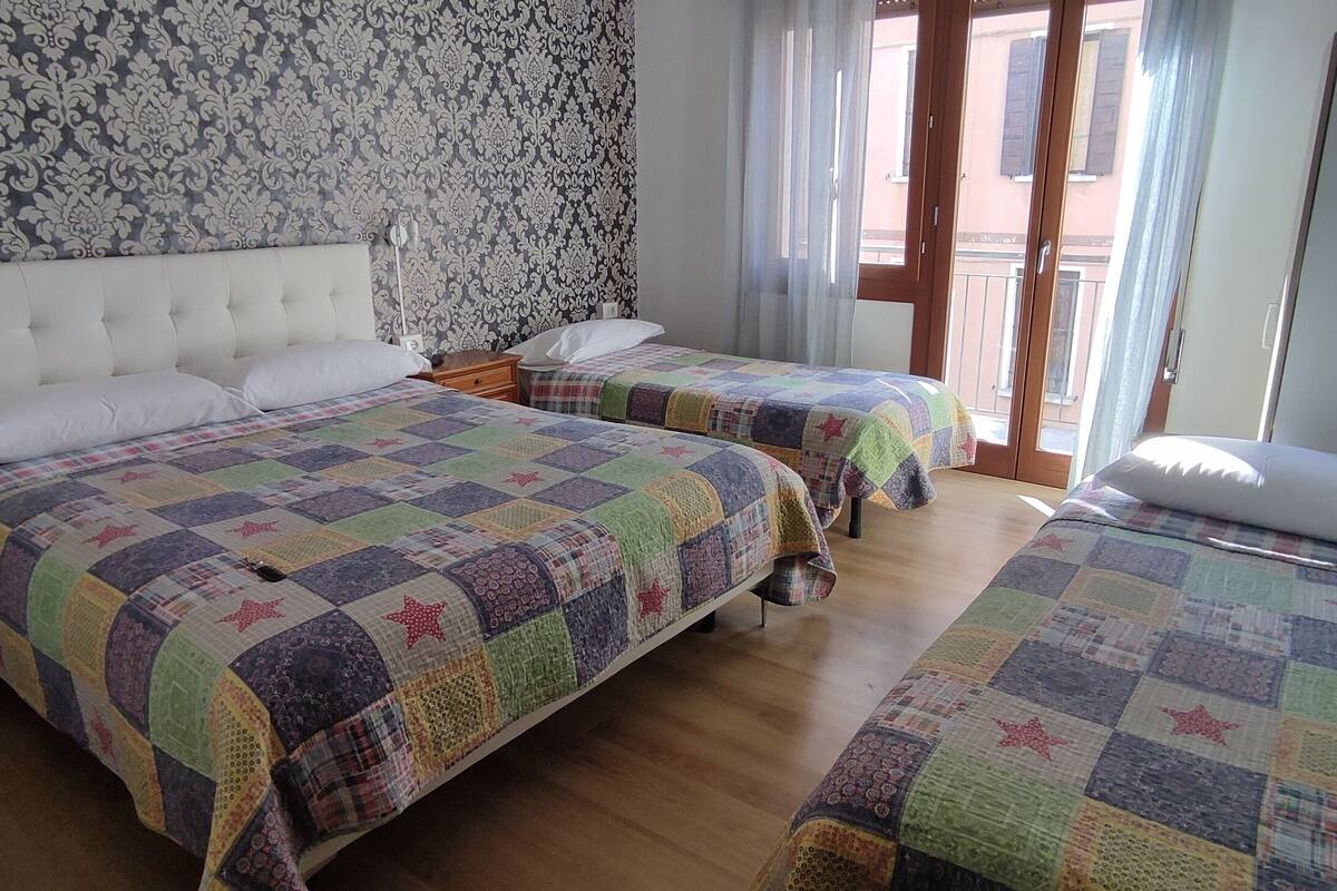 Une chambre avec deux lits, une grande fenêtre avec des rideaux et un papier peint à motifs.