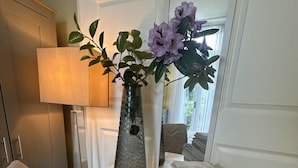 Una habitación con un amplio ventanal, un florero con flores y una lámpara.
