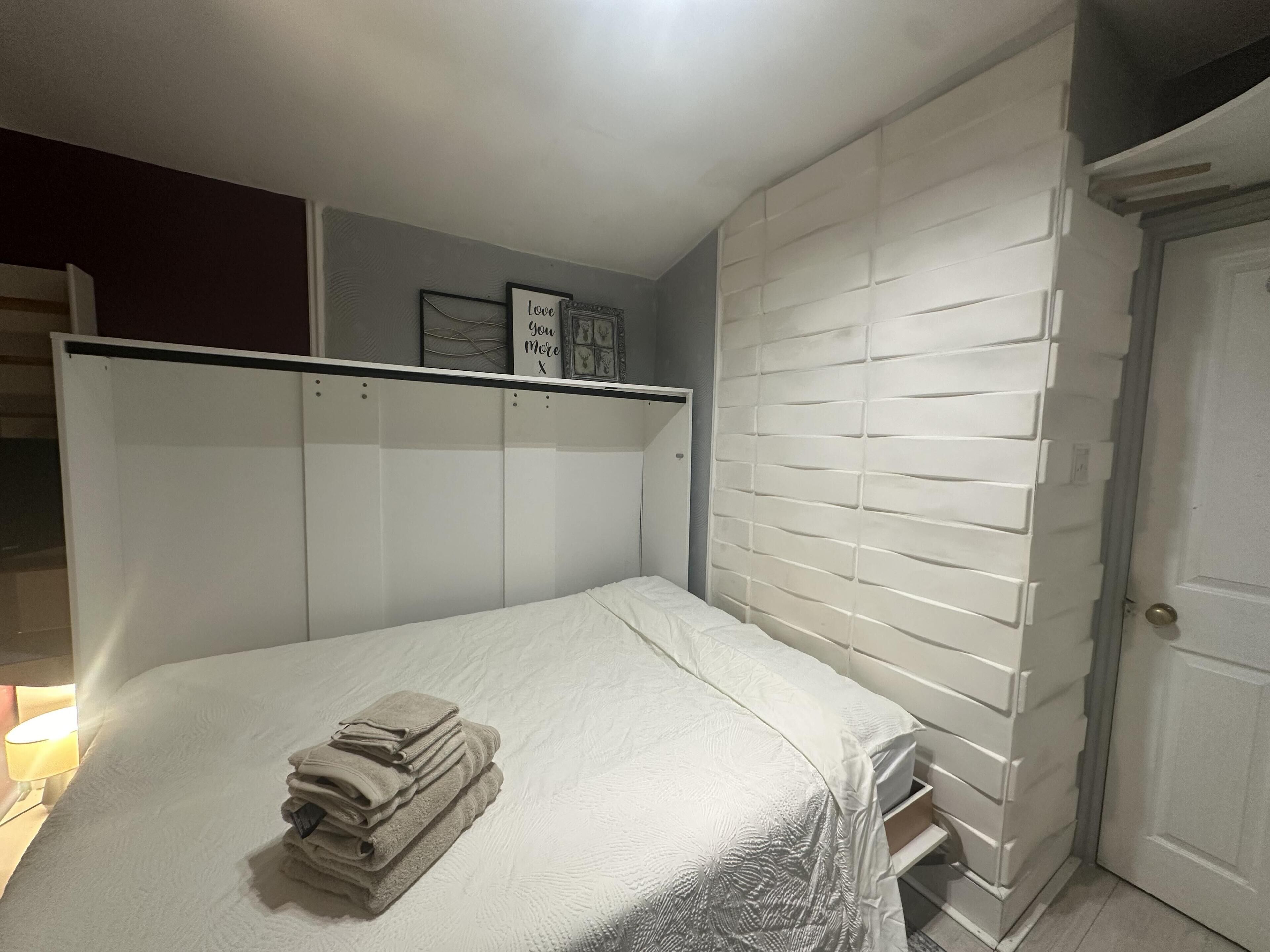 A bedroom with a bed, a white headboard, a door, and a wall with a white brick pattern.