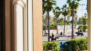A view from a balcony with a white balustrade, palm trees, and a street scene with people and horses. - Oliva Nova Club Sevilla VI Equestrian Center . Playa 400 Metros (OLIVA)