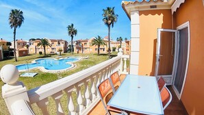 A balcony with a table and chairs, overlooking a swimming pool and palm trees. - Oliva Nova Club Sevilla VI Equestrian Center . Playa 400 Metros (OLIVA)