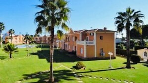 A row of two-story buildings with a central courtyard, palm trees, and a clear blue sky. - Oliva Nova Club Sevilla VI Equestrian Center . Playa 400 Metros (OLIVA)
