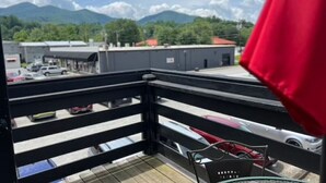 A balcony with a view of parked cars and buildings, a red umbrella, and mountains in the background.