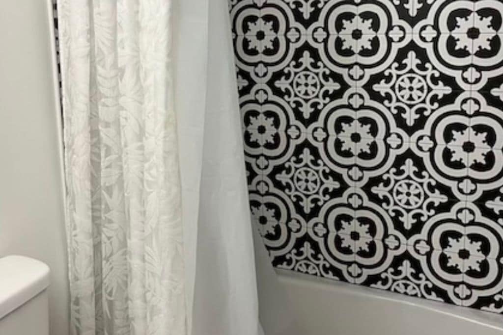 Un baño con pared de azulejos estampados, inodoro y cortina de ducha.
