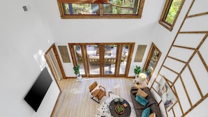 Amplia sala de estar con televisor grande, muebles de madera y vistas a un patio exterior a través de puertas de cristal.