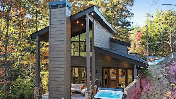 Una casa moderna con un gran ventanal, un jacuzzi y un patio con mobiliario exterior.