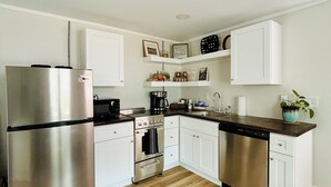 A modern kitchen with white cabinets, stainless steel appliances, and a wooden floor. - Walkable Cottage, Pet Friendly with Fenced Patio (Southern Pines)
