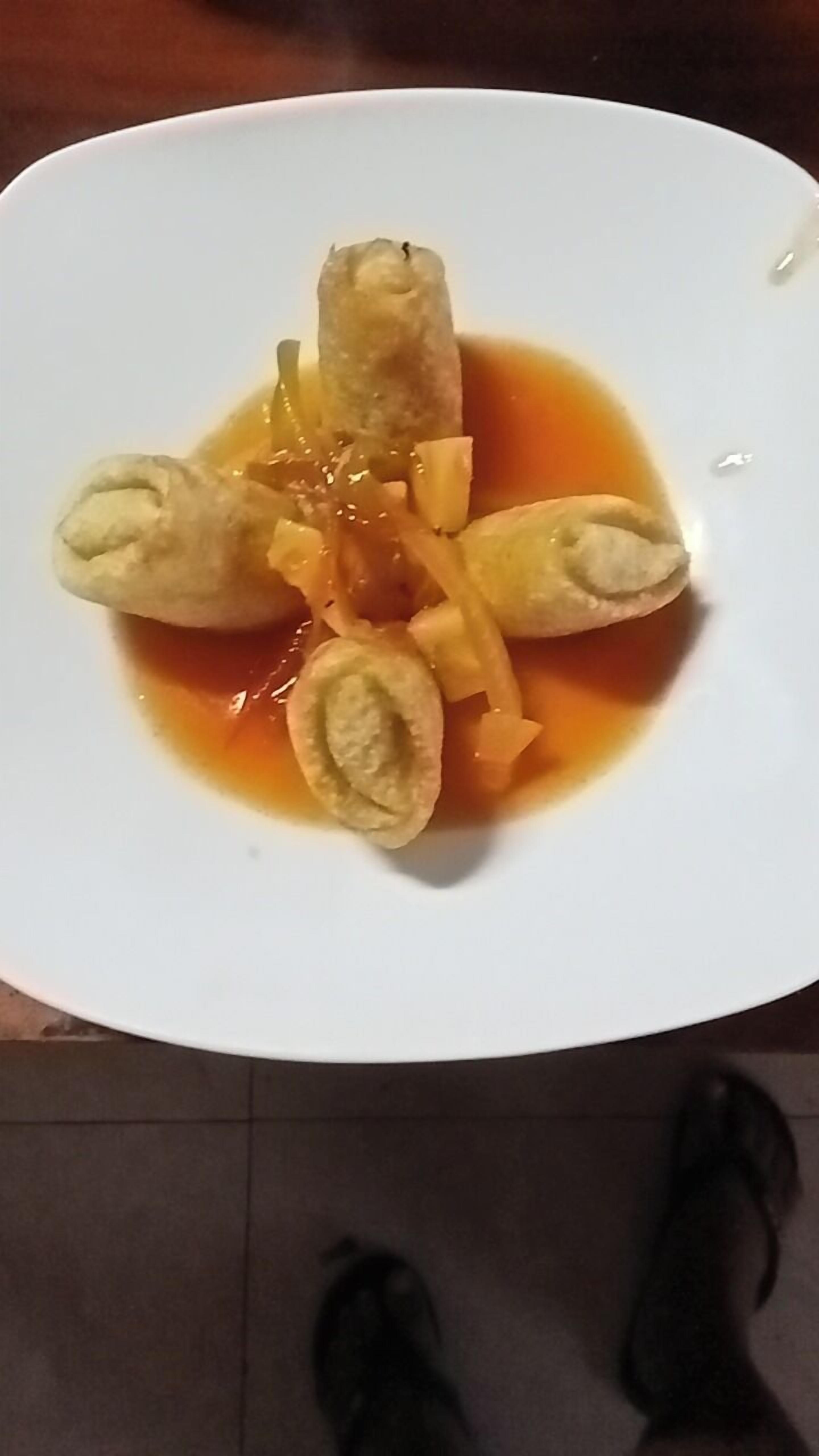 En vit tallrik med en maträtt som består av rullade ingredienser och en sås.
