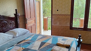 Ein Schlafzimmer mit einem großen Bett, einem hölzernen Kopfteil, einer Steudecke und Blick auf einen Balkon mit Grünpflanzen.