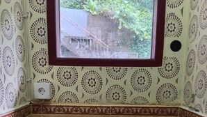 Ein Badezimmer mit einem runden Waschbecken, einem Fenster und Wandverkleidung mit Muster.