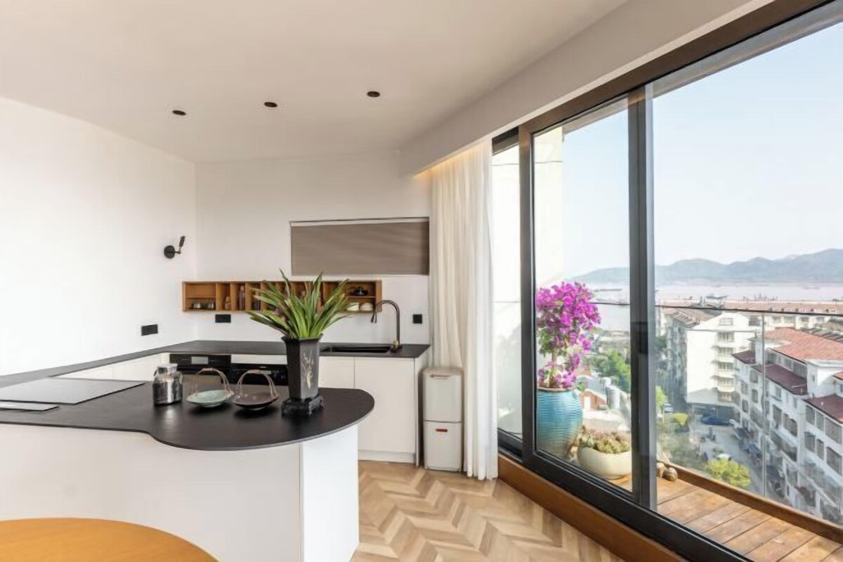 A modern kitchen with a black countertop, white cabinets, and a view of a cityscape through large windows.