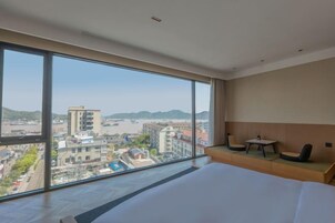 Habitación de hotel con un ventanal grande que ofrece vistas a la ciudad, una cama y una zona de estar con dos sillones y una mesita.