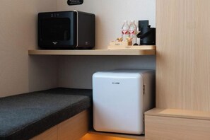 A compact kitchenette with a microwave, a small refrigerator, and a shelf with bottled water and snacks.